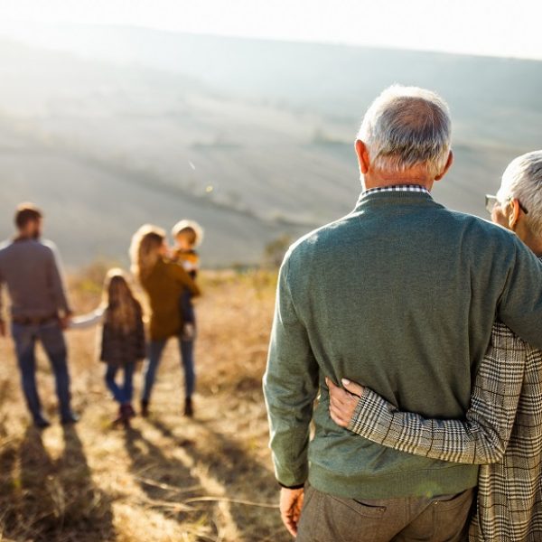 Back view of embraced grandparents enjoying while looking at their family on a field in autumn day.