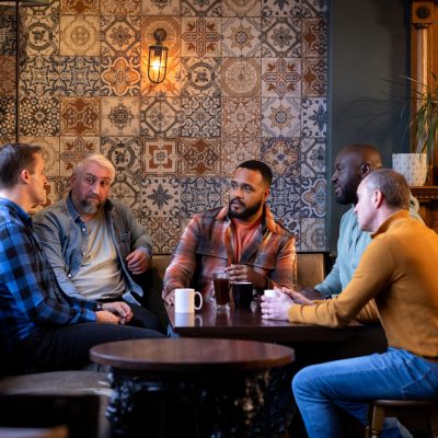 Three-quarter-length shot of five male friends having hot drinks in a rustic bar. They are having a serious conversation all wearing casual clothing. The bar/restaurant is located in Hexham.